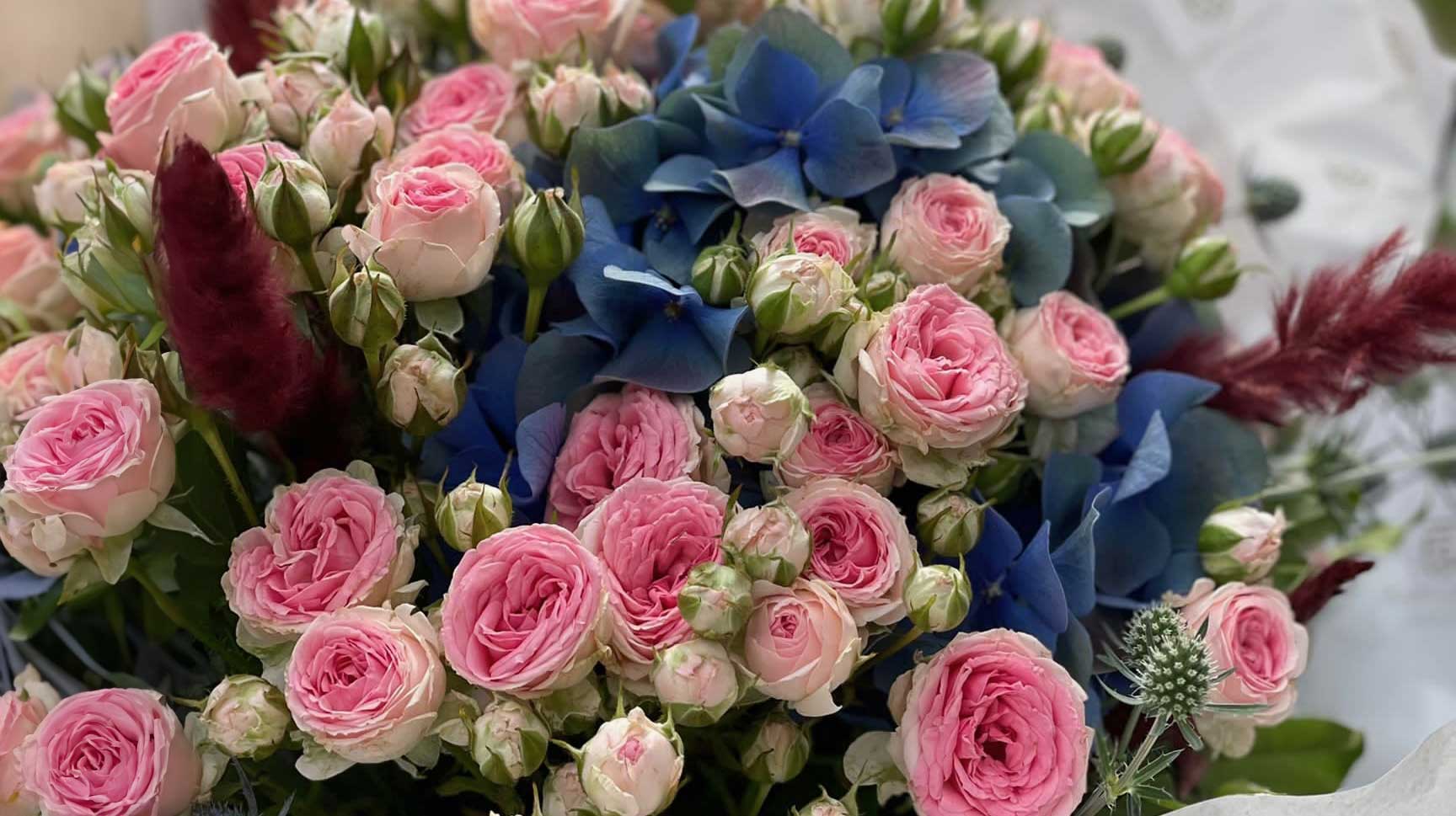 Ein wunderschöner Blumenstrauß aus rosa Rosen und blauen Hortensien, kombiniert mit grünen Akzenten und zarten Blättern, ideal für Frischblumenliebhaber, verfügbar bei JustFlower.ch.